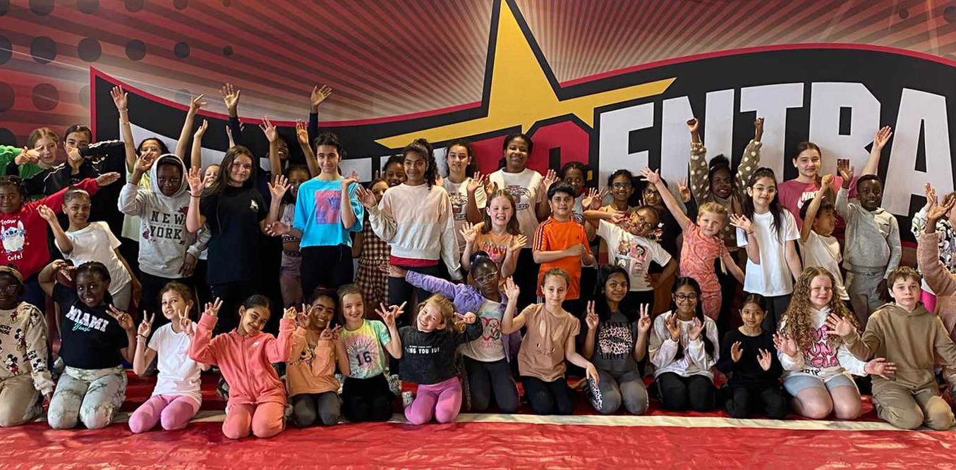 A group of young cheerleaders in front of a Talent Central banner, waving and smiling at the camera